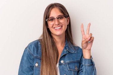 Beyaz arka planda izole edilmiş genç beyaz kadın neşeli ve kaygısız parmakları olan bir barış sembolü gösteriyor..
