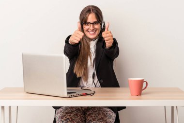 Beyaz arka planda evden işe dolaşan beyaz tenli genç bir kadın. Baş parmakları havada, bir şey için tezahürat yapıyor, destek ve saygı duyuyor..