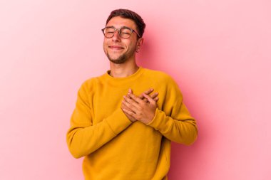 Sarı arka planda izole edilmiş dövmeleri olan genç beyaz bir adam gülüyor, ellerini yüreğine koyuyor, mutluluk kavramını koruyor..