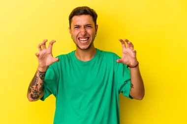 Sarı arka planda, pençelerini kedi taklidi yaparken gösteren dövmeleri olan genç beyaz bir adam. Saldırgan bir hareket..