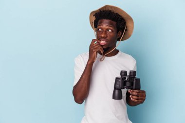 Genç Afrikalı Amerikalı bir adam mavi arka planda izole edilmiş dürbünler tutuyor. Bir şeyin fotokopi odasına baktığını düşünüyor..