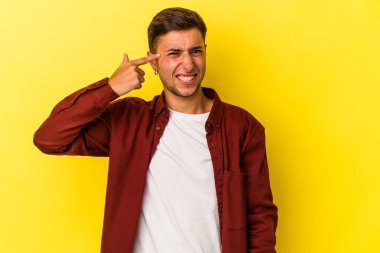 Sarı arka planda elleri kulaklarında, dövmeleri olan genç, beyaz bir adam..