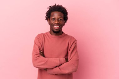 Pembe arka planda izole edilmiş genç bir Afro-Amerikan erkeği kendini güvende hissediyor ve kararlılıkla kollarını kavuşturuyor..