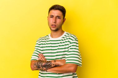 Sarı arka planda dövmeleri olan, sıkılmış, yorgun ve dinlenmeye ihtiyacı olan beyaz bir genç adam..