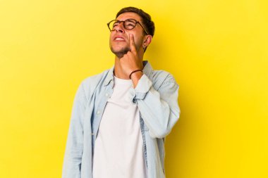 Sarı arka planda izole edilmiş dövmeleri olan genç, beyaz bir adam ağlıyor, bir şeyden mutsuz, acı ve kafa karışıklığı konsepti var..