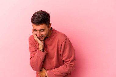 Sarı arka planda dövmeleri olan beyaz bir genç adam mutlu bir şekilde gülüyor ve ellerini karnının üstünde tutarak eğleniyor..