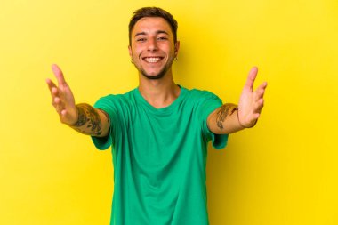 Sarı arka planda dövmeleri olan beyaz bir adam kameraya sarıldığı için kendini güvende hissediyor..