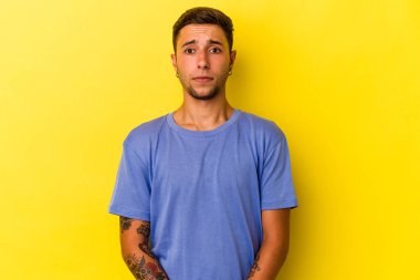 Sarı arka planda izole edilmiş beyaz dövmeli genç bir adam üzgün, ciddi yüzlü, mutsuz ve hoşnutsuz..