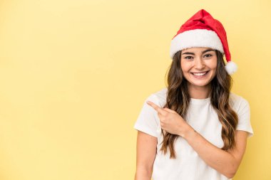 Sarı arka planda izole edilmiş bir şekilde Noel 'i kutlayan beyaz bir kadın gülümsüyor ve boş alanda bir şeyler gösteriyor..