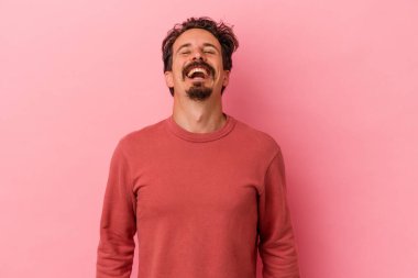 Genç beyaz adam pembe arka planda izole edilmiş rahat ve mutlu bir şekilde gülüyor, boynunda dişlerini gösteriyor..