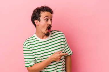 Kafkasyalı genç adam pembe arka planda izole edilmiş, başparmak uzakta, gülüyor ve kaygısız..