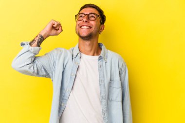 Sarı arka planda izole edilmiş dövmeleri olan genç beyaz adam zaferi, tutkuyu ve coşkuyu kutluyor..