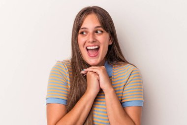 Beyaz arka planda izole edilmiş genç beyaz kadın ellerini çenesinin altında tutuyor, mutlu bir şekilde yana bakıyor..