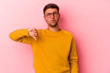 Sarı arka planda izole edilmiş beyaz dövmeli genç bir adam baş parmağını aşağı gösteriyor, hayal kırıklığı konsepti..