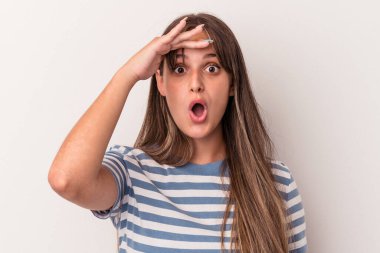 Beyaz arka planda soyutlanmış genç beyaz bir kadın çok uzaklara bakıyor ve elini alnına koyuyor..