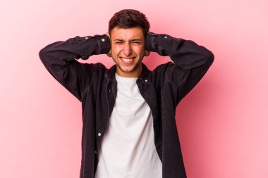 Sarı arka planda elleri kulaklarında, dövmeleri olan genç, beyaz bir adam..