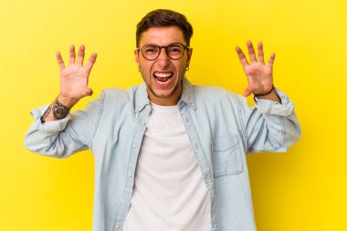 Sarı arka planda, pençelerini kedi taklidi yaparken gösteren dövmeleri olan genç beyaz bir adam. Saldırgan bir hareket..