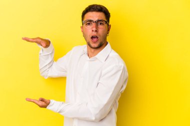 Sarı arka planda dövmeleri olan beyaz bir adam iki eliyle bir şey tutuyor, ürün sunumu..