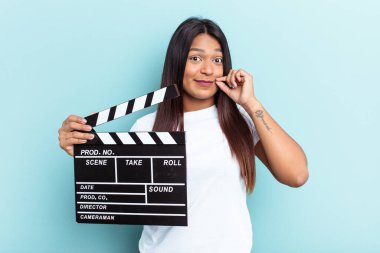 Genç Venezuelalı bir kadın mavi arka planda izole edilmiş bir klempon tutuyor. Parmakları dudaklarında bir sır saklıyor..