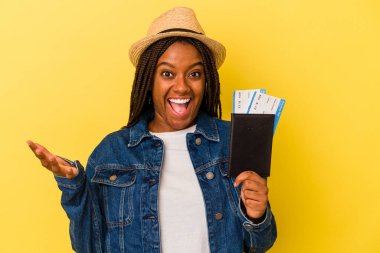 Sarı arka planda izole edilmiş pasaport taşıyan genç Afrikalı Amerikalı kadın hoş bir sürpriz alıyor, heyecanlı ve el kaldırıyor..