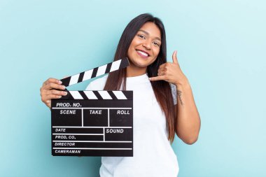 Genç Venezüellalı bir kadın mavi arka planda izole edilmiş bir el çırpma tahtası tutuyor. Cep telefonu hareketini parmaklarıyla gösteriyor..