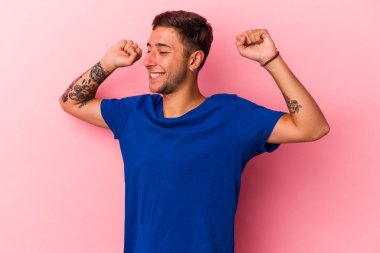 Sarı arka planda, özel bir günü kutlayan dövmeli, genç, beyaz bir adam atlıyor ve enerjiyle kollarını kaldırıyor..