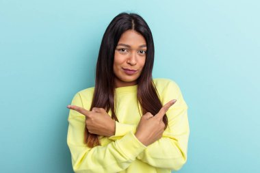 Genç Venezuelalı kadın mavi arka plan noktalarında izole edilmiş, iki seçenek arasında seçim yapmaya çalışıyor..