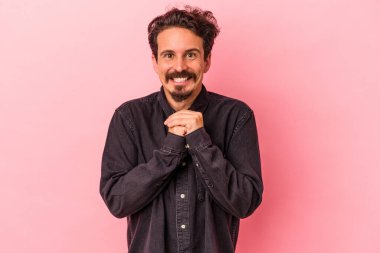 Pembe arka planda izole edilmiş genç beyaz adam ellerini çenesinin altında tutuyor, mutlu bir şekilde yana bakıyor..
