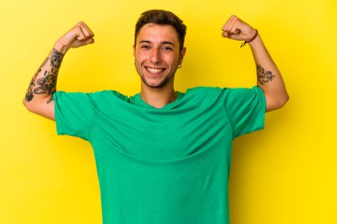 Sarı arka planda izole edilmiş beyaz dövmeli genç bir adam kollarıyla güçlü bir hareket gösteriyor, kadınsı gücün sembolü.