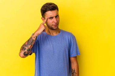 Sarı arka planda izole edilmiş beyaz dövmeli genç bir adam şakağı parmağıyla işaret ediyor, düşünüyor ve bir göreve odaklanıyor..
