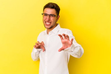 Sarı arka planda, pençelerini kedi taklidi yaparken gösteren dövmeleri olan genç beyaz bir adam. Saldırgan bir hareket..