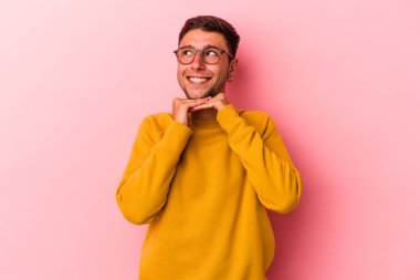 Sarı arka planda dövmeleri olan genç beyaz adam ellerini çenesinin altında tutuyor ve mutlu bir şekilde yan tarafa bakıyor..