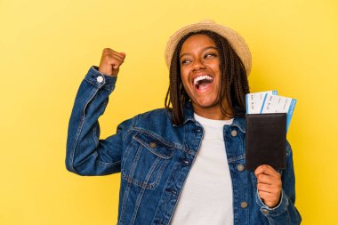 Pasaportu olan genç Afrikalı Amerikalı kadın sarı arka planda izole edilmiş zafer kazandıktan sonra yumruğunu kaldırıyor..
