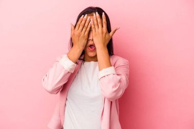 Pembe arka planda izole edilmiş genç Latin kadın yüzünün yarısını avuç içiyle örterek eğleniyor..
