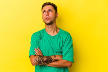 Sarı arka planda izole edilmiş dövmeleri olan genç beyaz bir adam tekrarlanan bir görevden yoruldu..