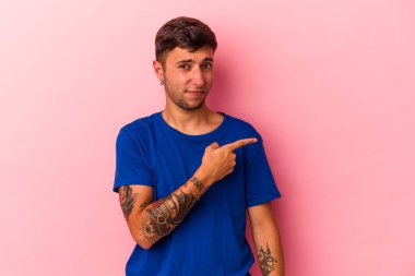 Sarı arka planda izole edilmiş, gülümseyen ve işaret eden, boş alanda bir şeyler gösteren beyaz dövmeli genç bir adam..