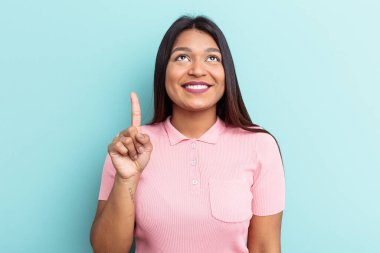 Mavi arka planda izole edilmiş genç Venezuelalı kadın iki parmağı da boş bir alan gösteriyor..