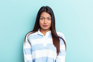 Genç Venezuelalı bir kadın mavi arka planda soyutlanmış üzgün, ciddi bir yüz, mutsuz ve hoşnutsuz.