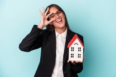 Mavi arka planda oyuncak evi olan genç bir iş kadını heyecanlı..