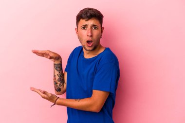 Sarı arka planda izole edilmiş beyaz dövmeli genç bir adam elleri arasında bir kopya alanı tutarken şok ve hayrete düştü..