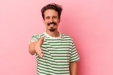 Pembe arka planda izole edilmiş genç beyaz adam gülümsüyor ve başparmağını kaldırıyor.