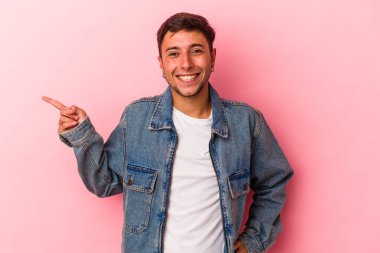 Sarı arka planda izole edilmiş dövmeleri olan genç beyaz adam işaret parmağıyla işaret ederek gülümsüyor..