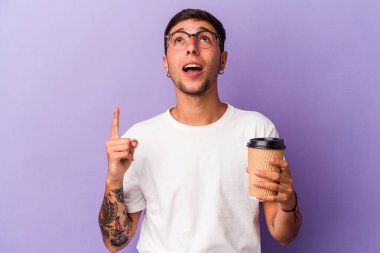 Elinde kahve tutan beyaz bir adam mor arka planda izole edilmiş ve ağzı açık bir şekilde yukarı işaret ediyor..