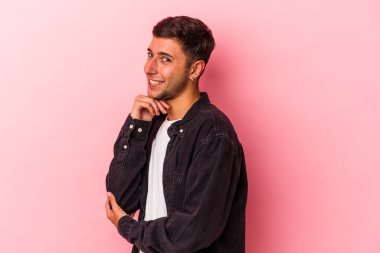 Sarı arka planda izole edilmiş, mutlu ve kendinden emin gülümseyen, elleriyle çenesine dokunan beyaz dövmeli genç bir adam..