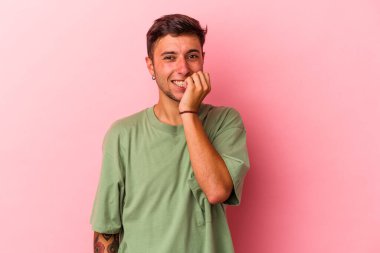 Sarı arka planda izole edilmiş, tırnak yiyen, gergin ve endişeli dövmeleri olan genç beyaz bir adam..