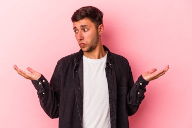 Sarı arka planda izole edilmiş beyaz dövmeli genç bir adam. Kafası karışmış ve omuz silkiyor..