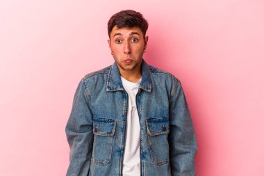 Sarı arka planda izole edilmiş dövmeleri olan beyaz genç bir adam omuzlarını silker ve gözleri açık kalır..