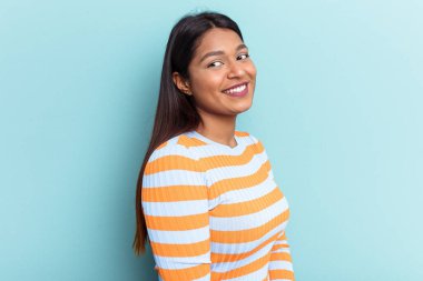 Genç Venezuelalı bir kadın mavi arka planda izole edilmiş. Gülümsüyor, neşeli ve keyifli görünüyor..