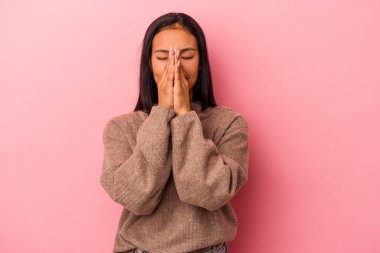 Pembe arka planda izole edilmiş genç Latin bir kadın. El ele tutuşup dua ediyor. Kendine güveniyor..