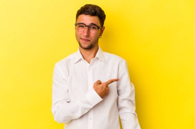 Sarı arka planda izole edilmiş, gülümseyen ve işaret eden, boş alanda bir şeyler gösteren beyaz dövmeli genç bir adam..